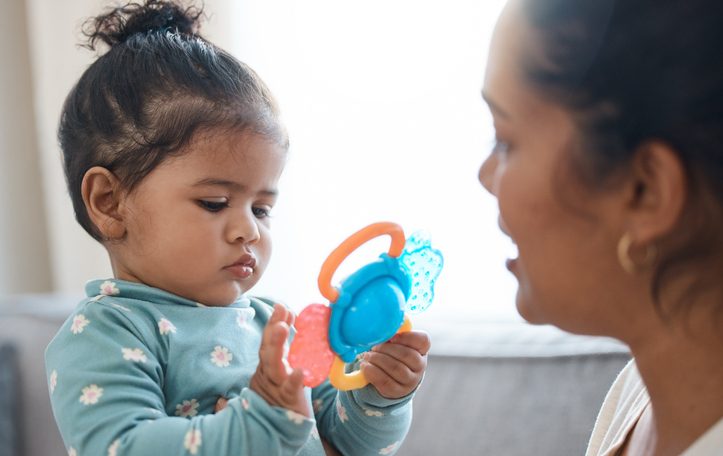 Toddler girl playing with colorful toy next to parent.
