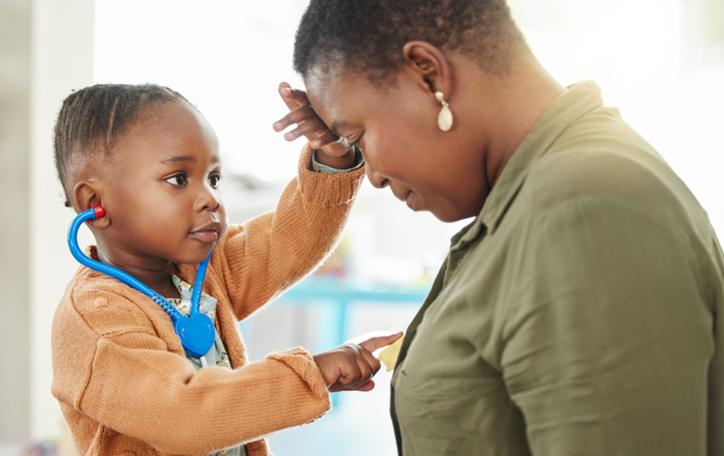African American boy playing Doctor with his mom, checking her forehead and pointing to her heart.