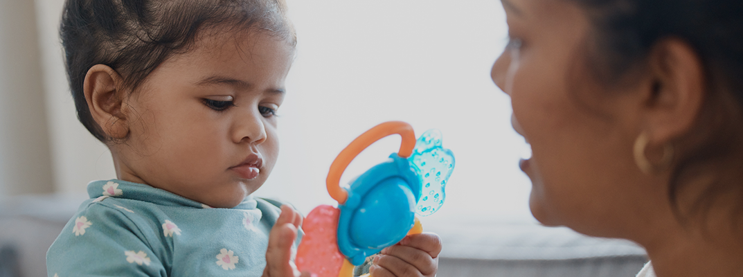 Toddler girl playing with colorful toy next to parent.
