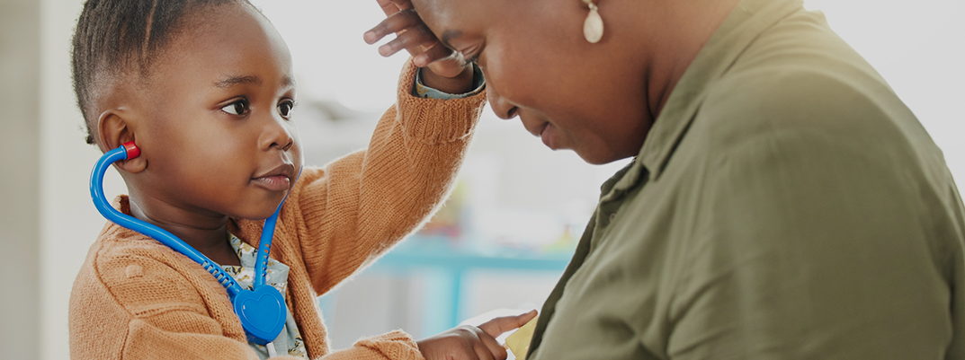 African American boy playing Doctor with his mom, checking her forehead and pointing to her heart.